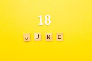 Top view of word 18 June calendar date made by wooden cubes on yellow color background photo