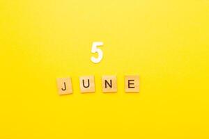 Top view of word 5 June calendar date made by wooden cubes on yellow color background photo