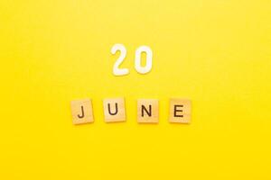 Top view of word 20 June calendar date made by wooden cubes on yellow color background photo