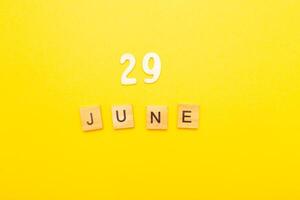 Top view of word 29 June calendar date made by wooden cubes on yellow color background photo
