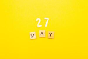 Top view of word 27 May calendar date made by wooden cubes on yellow color background photo