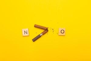 Top view of broken cigarette with the word no on a yellow background closeup photo