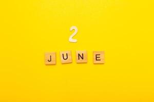 Top view of word 2 June calendar date made by wooden cubes on yellow color background photo