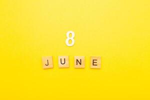 Top view of word 8 June calendar date made by wooden cubes on yellow color background photo