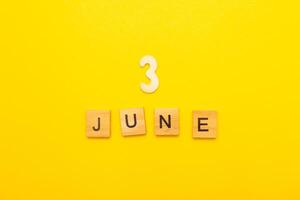 Top view of word 3 June calendar date made by wooden cubes on yellow color background photo