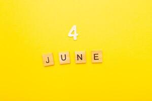 Top view of word 4 June calendar date made by wooden cubes on yellow color background photo
