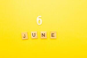Top view of word 6 June calendar date made by wooden cubes on yellow color background photo