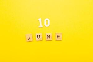 Top view of word 10 June calendar date made by wooden cubes on yellow color background photo