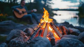 Cozy bonfire surrounded by rocks with a guitarist playing by the lakeside at twilight photo