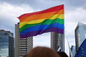 Pride Flag in Urban Setting. A vibrant rainbow flag waves against a city skyline, photo