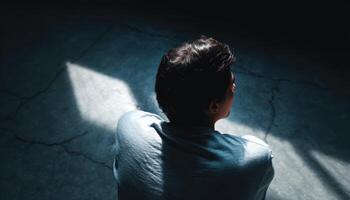 Person contemplating in a dark room with light cracks emotional reflection indoor environment photo