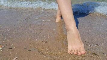 Barefoot walking on a sandy beach next to gentle sea waves and creating a heart shape in the sand video