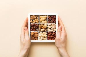 Young woman holding box with different nuts, closeup. Close up, copy space, top view, flat lay. Walnut, pistachios, hazelnuts and cashews photo