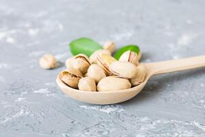 Close-up tasty pistachio nuts in spoon with leaves on table background. Top view. Flat lay photo