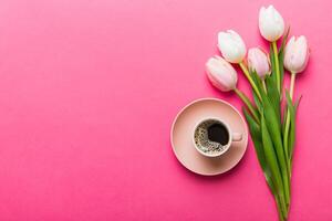 Spring background with flowers, cup of coffee and a bouquet of pink and white tulips on colored table background with place . Copy space top view photo