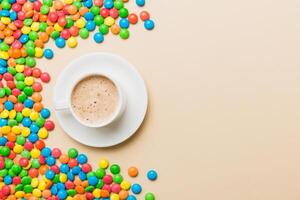 Coffee cup with chocolates and colored candy. Top view on table background photo