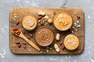 Glass jar with peanut butterin plate on table background, top view space for text photo