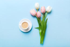 Spring background with flowers, cup of coffee and a bouquet of pink and white tulips on colored table background with place for text. top view photo
