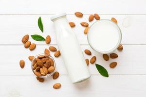 Top view the almond milk the glass bottle with almond nuts on the colored table. top view photo