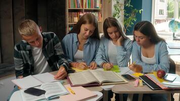 Caucasian four teenagers writing homework preparing classmates learn in library school pupils students with book prepare exams in academy college study together learning education talking teamwork photo