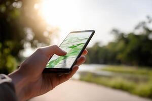 Hand holds smartphone with map app, outdoors. Sunlight filters through trees photo
