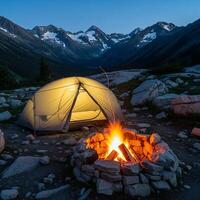 Mountain Camping at Dusk with Illuminated Tent and Campfire photo