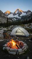 Campfire Glows Near Tent with Mountain Views at Dusk in the Wilderness photo