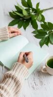 Writing in a Journal with Tea and Greenery on a Wooden Table photo
