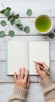 Top-down view of hands writing in a notebook with tea and eucalyptus leaves photo