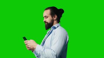 Young carefree man checking his mobile phone against green screen backdrop, being connected online on social network apps or texting messages. Social media platforms. Camera A. video