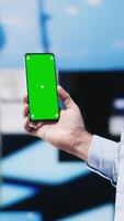 Vertical Casual stylish guy browsing his smartphone against green screen background, connected online on social network platforms or texting messages. Young adult focused on social media apps. Camera A. video