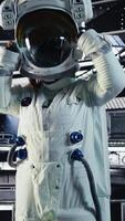 Vertical Portrait of smiling astronaut inside high tech spacecraft, holding equipment case during routine mission check. Happy starship crew member standing near monitor showing Mars data video