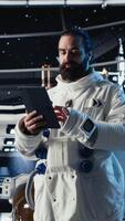 verticale femelle astronaute dans scaphandre chèques Humain expansion dans espace mission Les données sur tablette à l'intérieur vaisseau spatial. femme dans vaisseau prépare pour expédition justificatif longue terme humanité survie, caméra b video