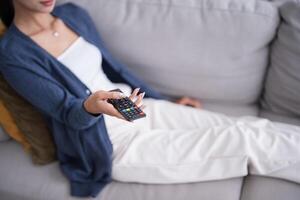 Asian woman Watching smart TV and using remote controller Hand holding television audio remote control at home with the remote control television. photo