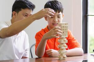 Asian father and son playing wood blocks game Carefree, kid playing wood blocks game building constructor from blocks with father at home. photo
