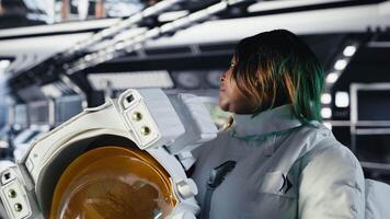Portrait of jolly female astronaut holding helmet inside space station after completing surface mission on unfamiliar planet. Smiling african american cosmonaut preparing for return to Earth, camera B video