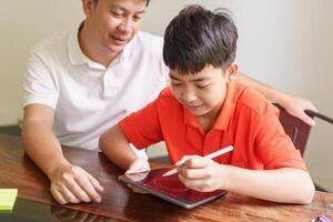 a man and a boy sitting at a table using tablat photo