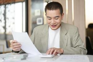 asian man in suit sitting at table with paper and calculator photo