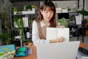 a woman is sitting at a desk with a notebook and a laptop photo