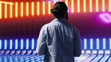 Casual young guy looking around at the glowing neon lights with vibrant colors, enjoying the futuristic cyberpunk atmosphere. Showcasing urban style and creativity in a nightlife scene. Camera A. video