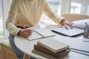 Student woman is writing in her notebook while sitting at a table with a laptop and a notebook photo