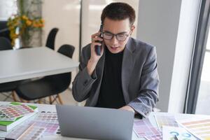 a businessman artist in a suit talking on the phone while using a laptop photo