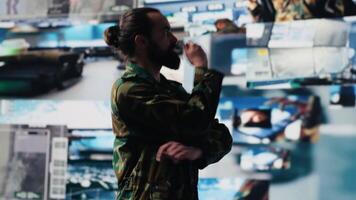 Male army officer operates from a mission command center with digital tech, monitoring satellite intelligence for modern combat strategy. Secure communications in active operations. Camera A. video