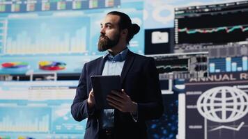 Young entrepreneur contemplating about a strategy to increase firm revenue while he evaluates infographics and fintech insight with digital tools. Ensuring his long term success and growth. Camera A. video