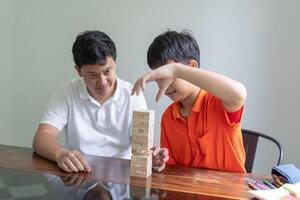 Asian father and son playing wood blocks game Carefree kid playing wood blocks game building constructor from blocks with father at home. photo