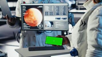 Astronaut monitoring system diagnostics on isolated screen smartphone during space mission. Teamworking cosmonauts using mockup mobile phone during cosmic expedition, camera B video
