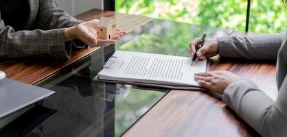 two people sitting at a table holding home model with a pen and paper photo