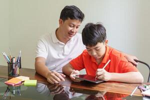 Asian father and son using tablet teaching son to drawplaying with digital tablet at desk fatherhood photo