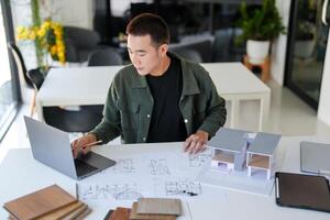 a man working on a laptop in front of a desk with architectural plans photo