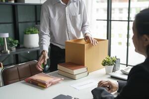 a man is opening a box with papers and a woman is sitting at a desk photo